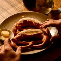 Someone's hands are ready to grab the huge pretzel that sits on a plate in Hahndorf