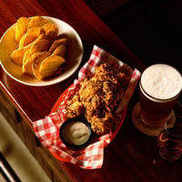 Chips, fried chicken in a bucket and a frothy beer sit on a table at NOLA