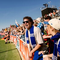 Sign and flags fly high in the stands which cheer on the players on the football field during AFL Gather Round