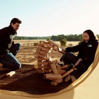 A couple sit on the deck of their Bukirk Glamping tent as their giant game of jenga topples over 