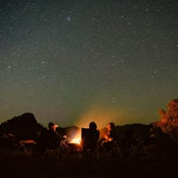 A group sit in deck chairs around a fire and under the stars on the ridgetop sleepout at Arkaroola 