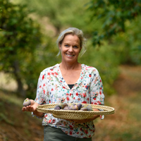 a woman holds a bowl of figs with fig trees in the background